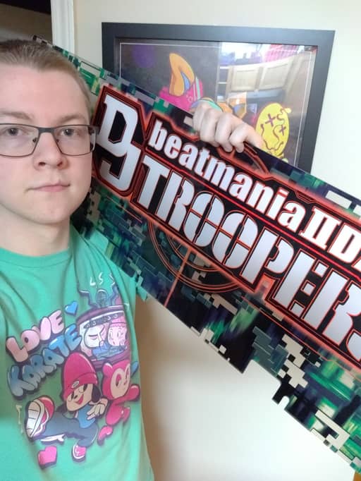 photo of clue holding an arcade marquee for 'beatmania iidx dj troopers'